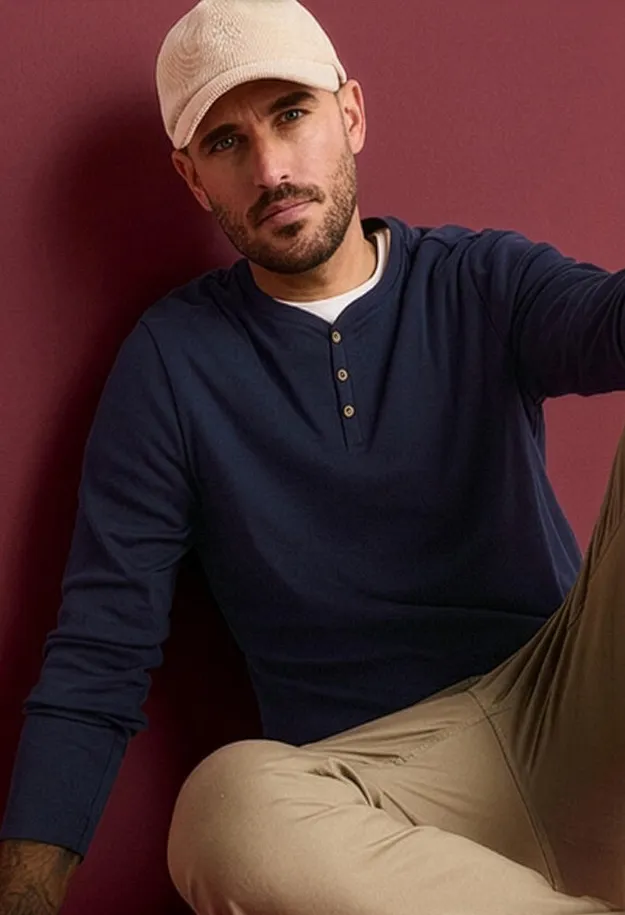Der Mann tr&auml;gt eine beige Kappe, ein marineblaues Henley-Shirt und beige Hosen.