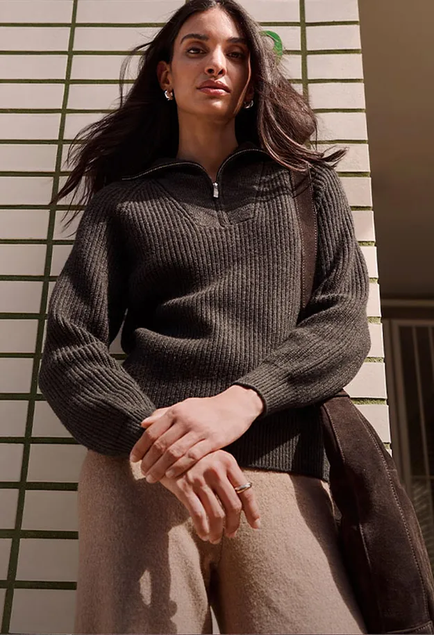 Dunkler Rippstrickpullover mit Rei&szlig;verschluss, helle Hose und braune Wildledertasche.