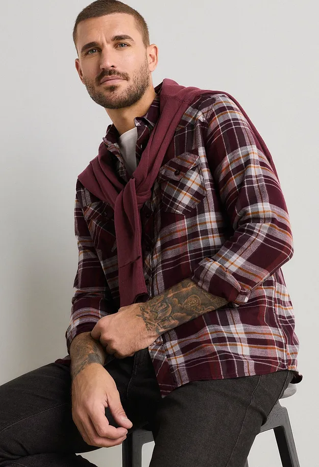 Kariertes Hemd in Bordeauxrot, dunkle Jeans und passender Pullover.