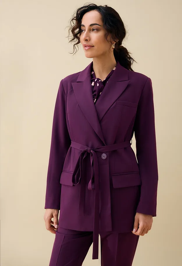 Eleganter violetter Blazer mit G&uuml;rtel und passender Hose, dazu eine gepunktete Bluse.