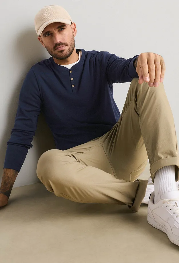 Beige M&uuml;tze, blaues Henley-Shirt, beigefarbene Hose und wei&szlig;e Sneaker.