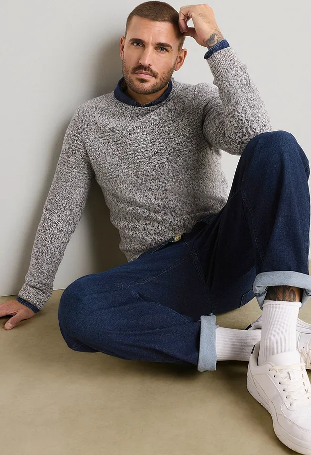 Grauer Strickpullover &uuml;ber blauem Hemd, dunkle Jeans, wei&szlig;e Socken und Sneaker.