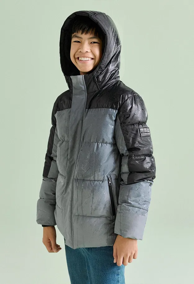Der Junge tr&auml;gt eine stylische zweifarbige Steppjacke mit Kapuze