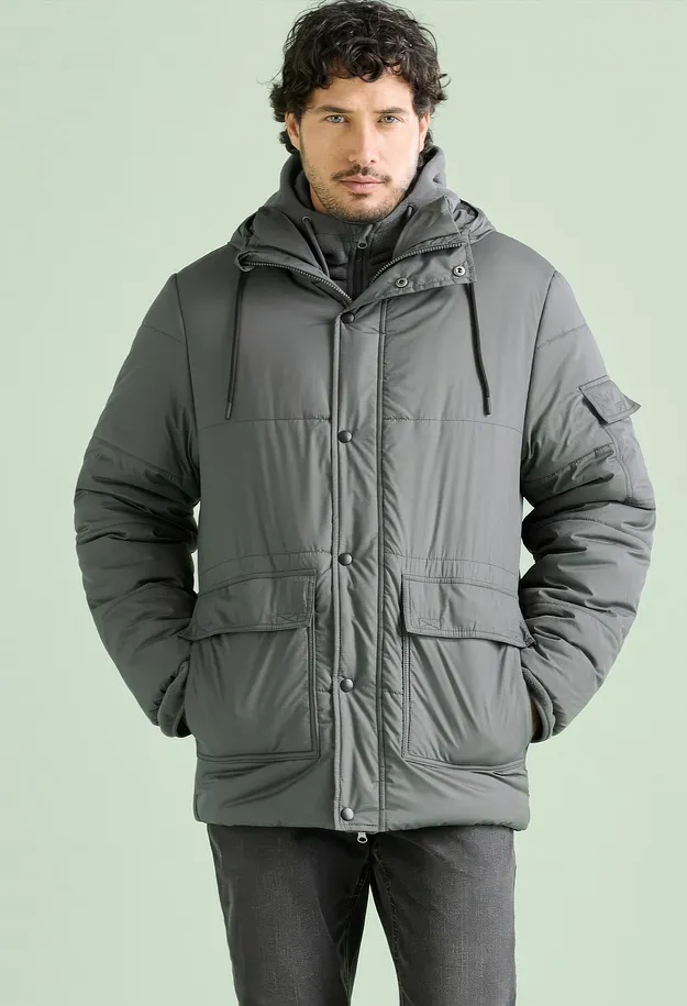 Ein Mann tr&auml;gt eine stilvolle, graue Steppjacke mit Kapuze und praktischen Taschen.