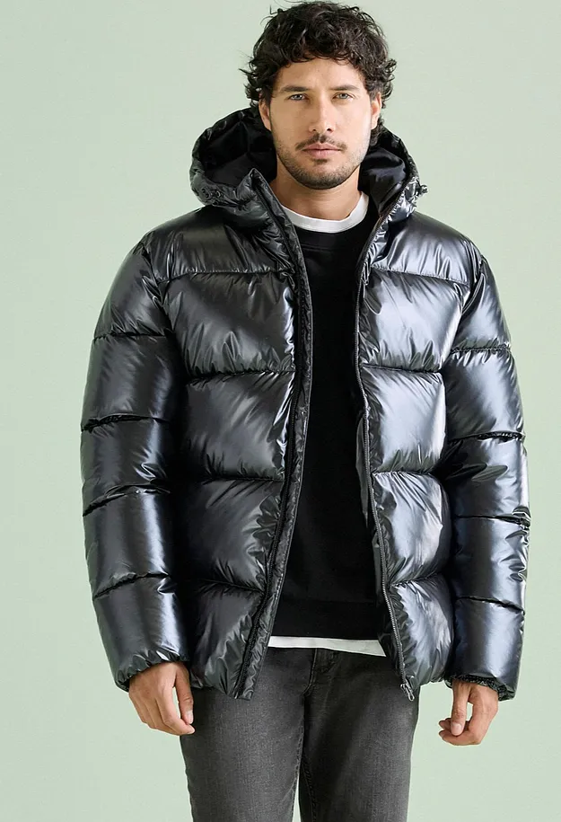Der Mann tr&auml;gt eine stylische, gl&auml;nzende schwarze Pufferjacke mit Kapuze und dunkler Hose.