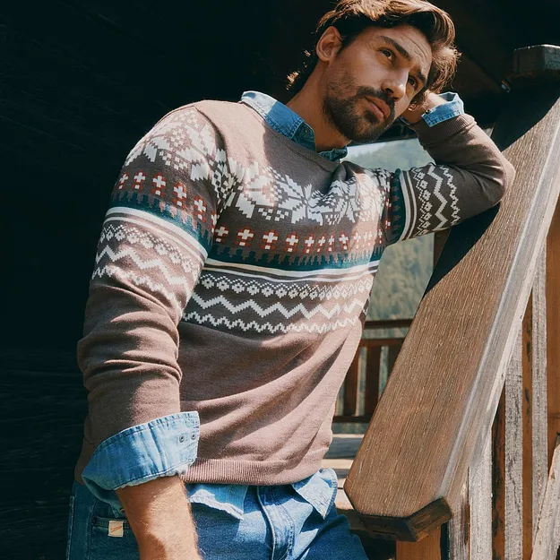 Der Mann tr&auml;gt einen gemusterten Pullover &uuml;ber Jeanshemd und blauer Jeans.