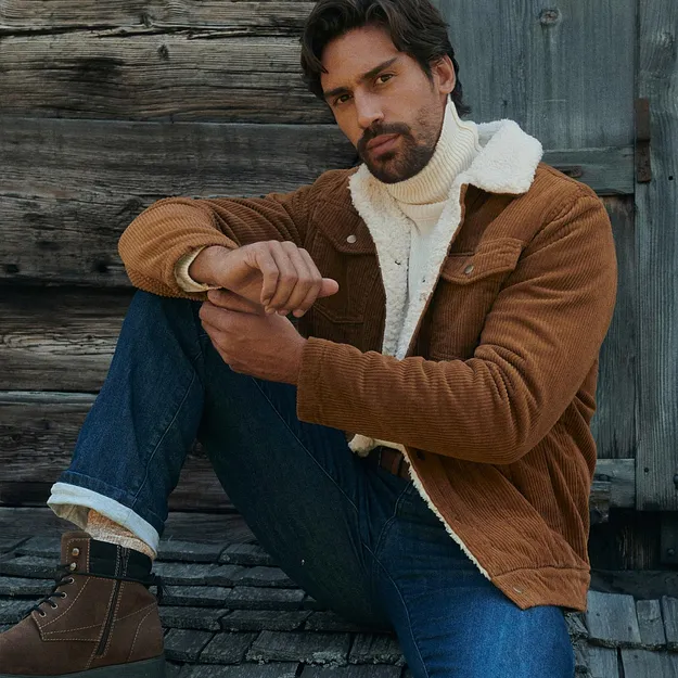 Mann in brauner Cordjacke, wei&szlig;em Rollkragenpullover, Jeans und warmen Stiefeln.