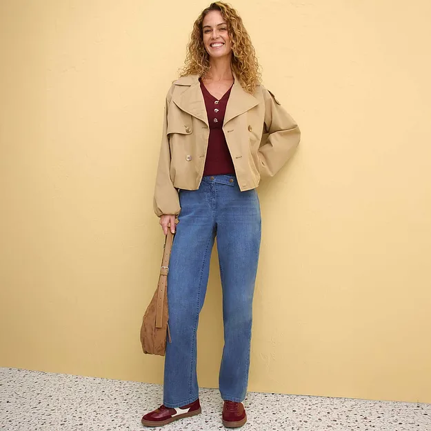 Veste beige port&eacute;e sur un top rouge bordeaux, associ&eacute;e &agrave; un jean bleu.