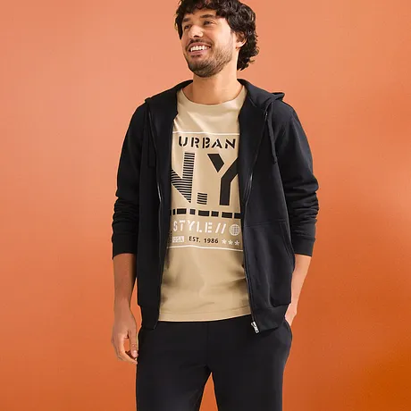 Lässiger Look mit beigem T-Shirt, schwarzer Kapuzenjacke & dunklen Sweat-Shorts.