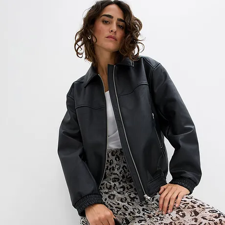 Schwarze Lederimitat-Jacke mit Reißverschluss, kombiniert mit weißem Shirt und gemustertem Rock.