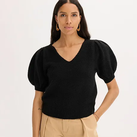 Schwarzer Pullover mit Puffärmeln und V-Ausschnitt, kombiniert mit beiger Hose.
