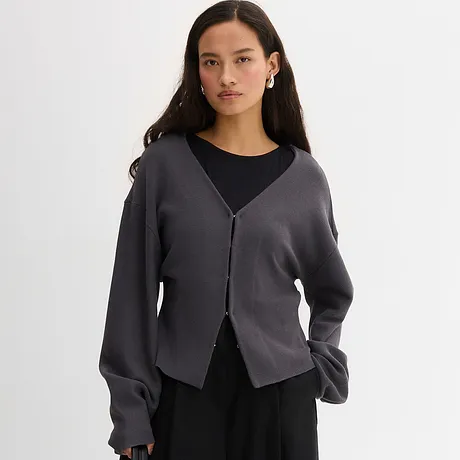 Elegante graue Strickjacke über schwarzem Top. Lässiger Look mit V-Ausschnitt und Knopfleiste.