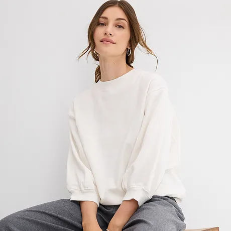 Weißes Oversize-Sweatshirt mit weiten Ärmeln, kombiniert mit einer grauen Hose.