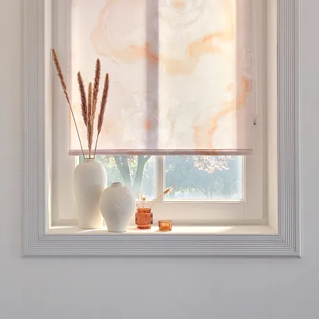 Sonnendurchflutetes Fenster mit zartem Rollo, davor eine Vase mit getrockneten Gräsern.