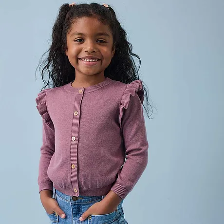 Gilet rose en maille avec ruchés sur les épaules et jean bleu.