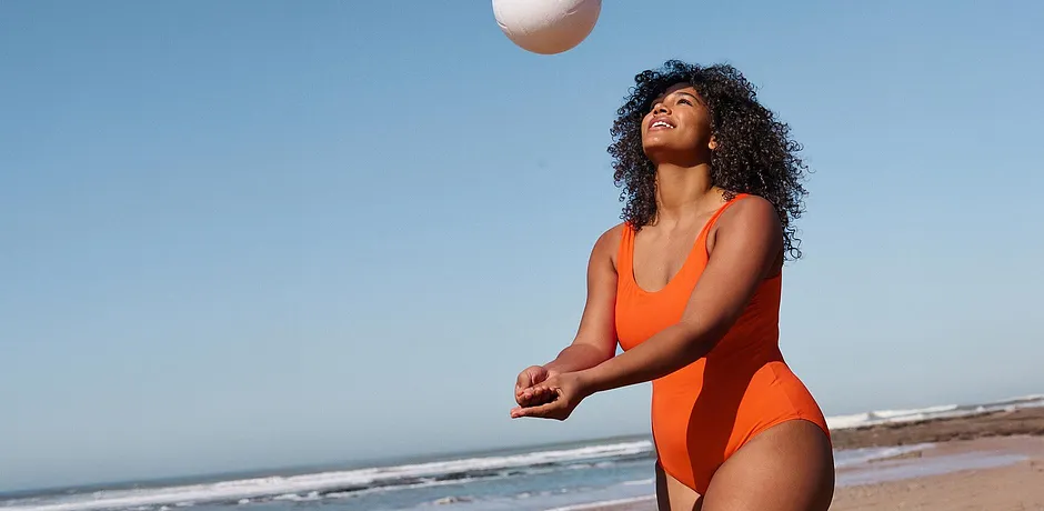 Leuchtend orangefarbener Badeanzug am Strand. Sportliche Eleganz unter strahlend blauem Himmel.