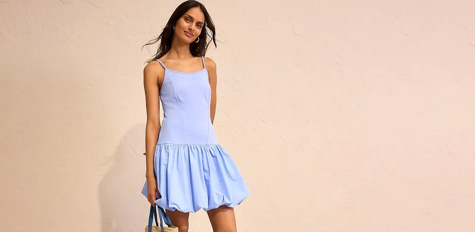 Sommerliches hellblaues Kleid mit dünnen Trägern und ausgestelltem Rock, kombiniert mit Strohhandtasche.
