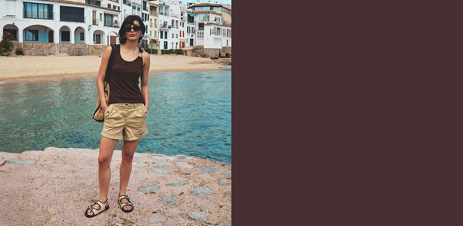Femme à la plage, vêtue d'un débardeur noir, d'un short beige et d'une paire de sandales.