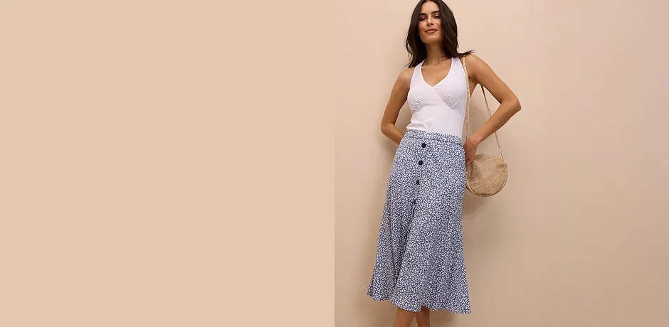 Top sans manches blanc associé à une jupe midi imprimée, le tout complété par un sac en paille pour un look estival chic.