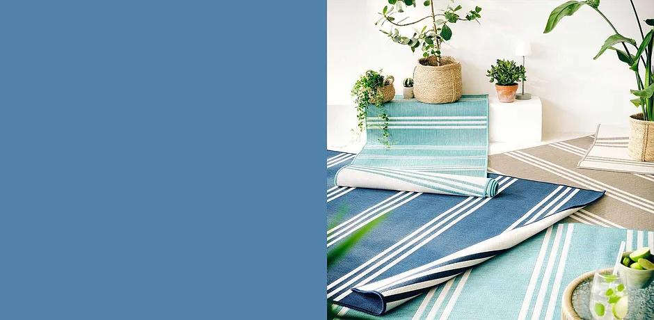 Table décorée de tapis d’extérieur rayés dans des tons bleus et verts, avec des plantes vertes.