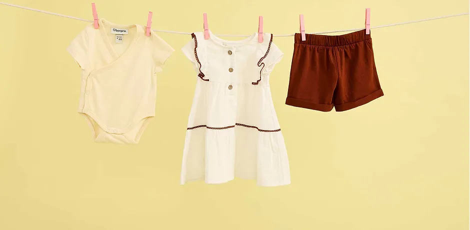 Sommerliche Babykleidung an der Wäscheleine: Body, weißes Kleid und braune Shorts für warme Tage.