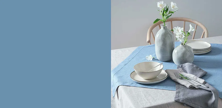 Elegantes Geschirr in sanften Pastelltönen auf hellblauem Tischtuch.