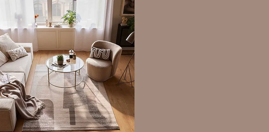 Gemütliches Wohnzimmer mit beigem Sessel, flauschiger Decke und stilvollem Teppich in warmen Erdtönen.