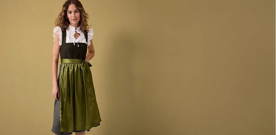 Ein traditionelles Dirndl mit weißer Bluse, schwarzem Mieder und grünem Rock wird präsentiert.