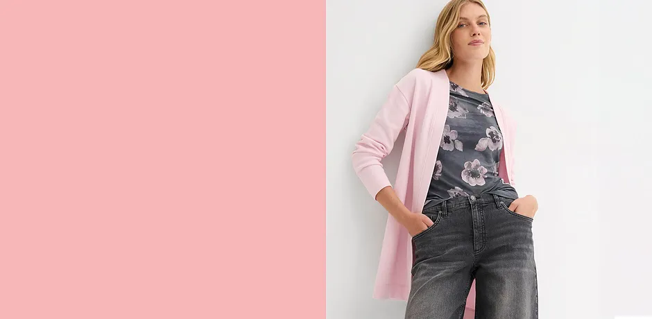 Langer rosa Mantel über dunkler Jeans. Eleganter Kontrast zwischen hellen und dunklen Farbtönen.