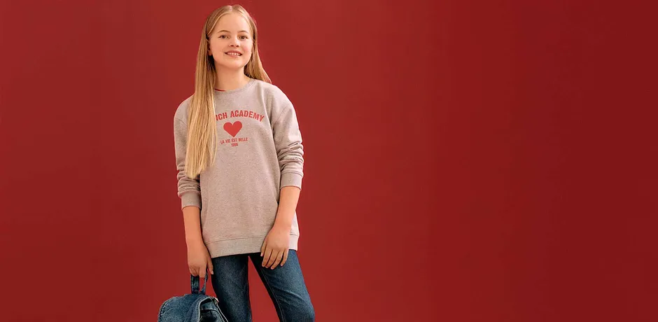 Pull gris avec inscription et cœur rouge imprimé, jean bleu et un sac en jean pour l'accessoire.