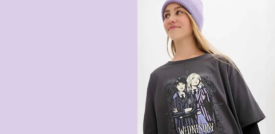 Un bonnet lilas et un T-shirt gris oversize orné d'un motif gothique sombre signent le look urbain streetwear.