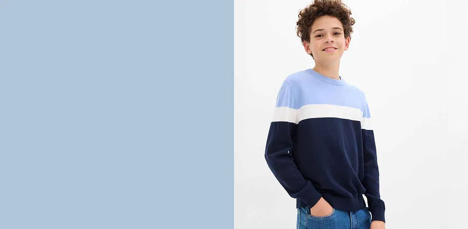 Un pull tricolore dans des tons de bleu, un jean clair et une casquette de baseball bleue composent le look décontracté.