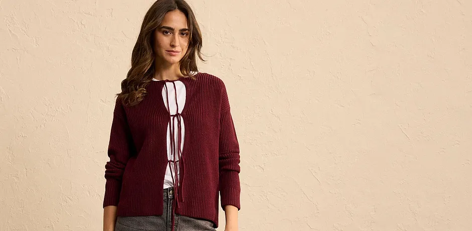 Gilet rouge bordeaux en maille avec laçages par dessus un haut blanc.