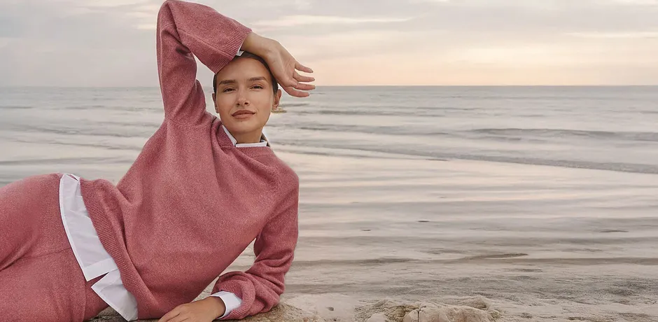 Frau in rosa Strick-Hoodie am Meer, gemütlicher Loungewear-Look.