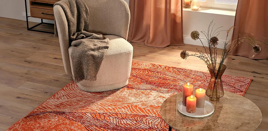 Sessel mit flauschiger Decke auf leuchtendem Teppich. Warme Herbstfarben schaffen behagliche Atmosphäre.