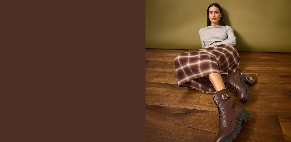 Pull gris, jupe à carreaux et bottes marron.