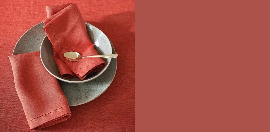 Tischdekoration in Korallrot: Serviette auf grauem Teller mit goldenem Besteck.
