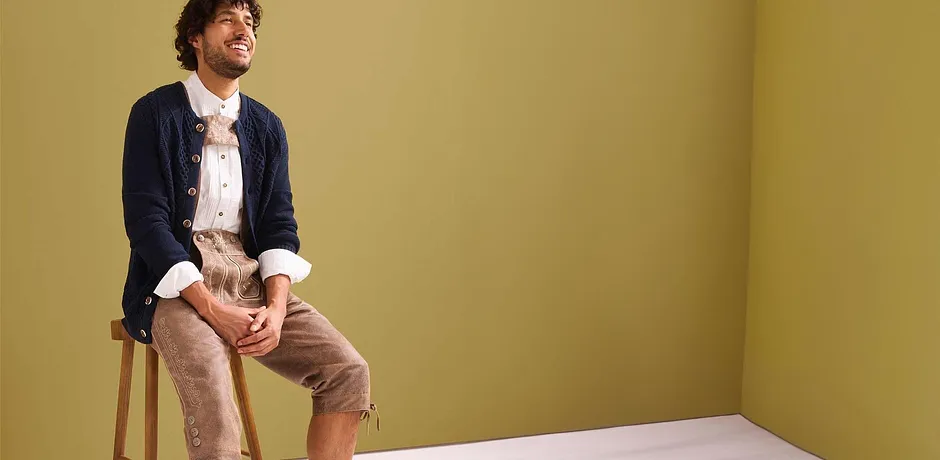 Marineblaue Strickjacke über hellem Trachtenhemd, kombiniert mit beigen Lederhosen. 