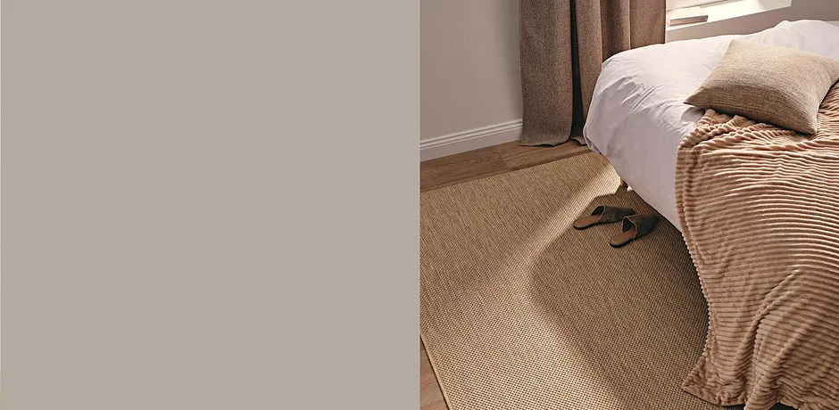 Lässige Pantoffeln ruhen auf natürlichem Sisalteppich neben einem Bett mit gestreifter Decke.
