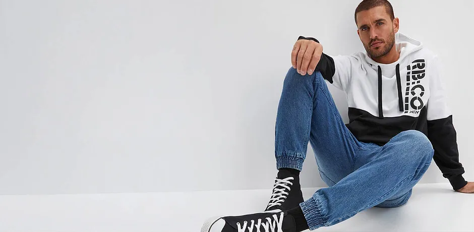 Look décontracté composé d'un jean, un pull à capuche bicolore et des baskets.