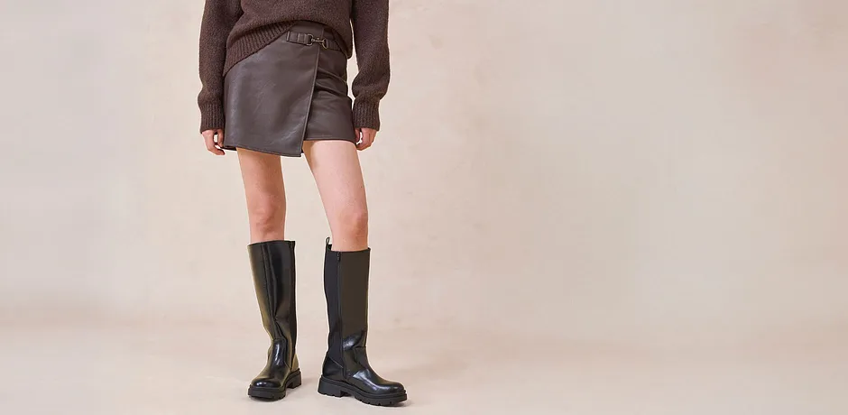 Jupe enduite et bottes hautes associées à un pull marron.