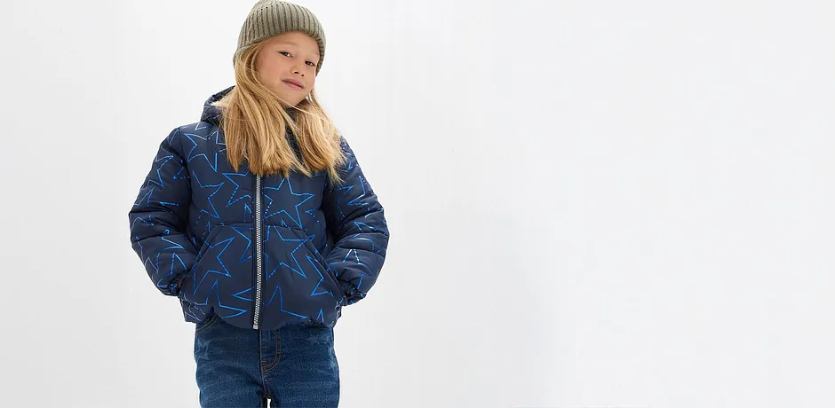 Gesteppte blaue Jacke, Jeans und eine kuschelige grüne Mütze.