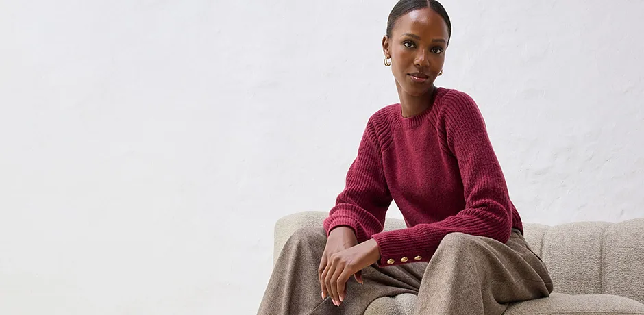 Pull rouge avec pantalon beige sur un canapé clair.