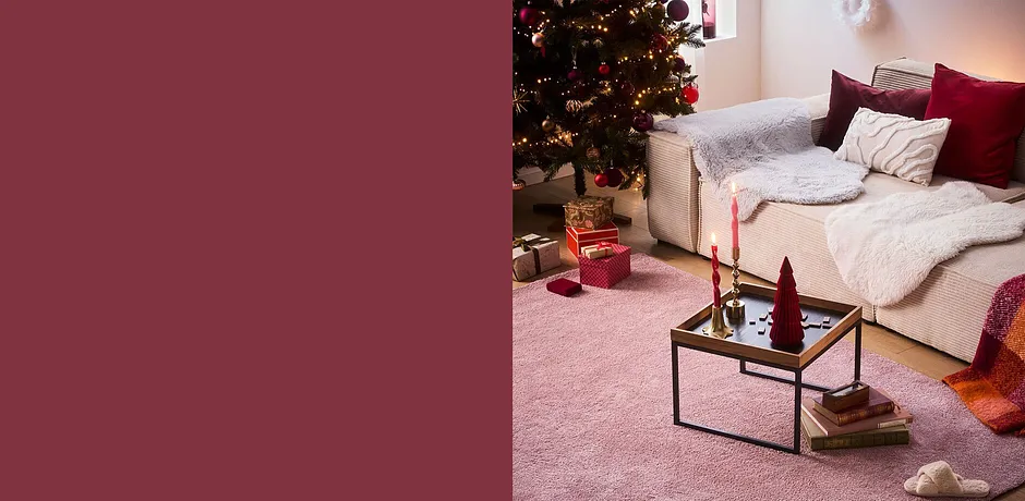 Coin salon cocooning avec couverture et coussins douillets. Un sapin de Noël et une ambiance de fête caractérisent la pièce.