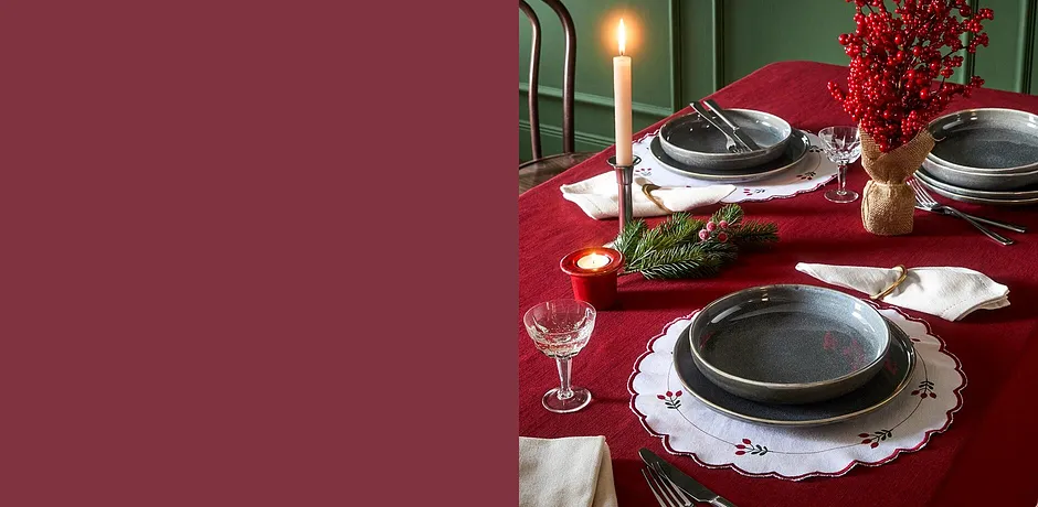Table festive avec une nappe rouge, des napperons blancs et des couverts de couleur argentée.