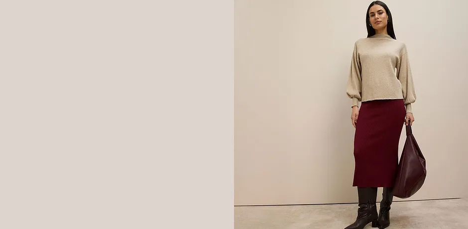 Pull beige, jupe en maille bourgogne, bottes marron et grand sac à main de couleur bordeaux.