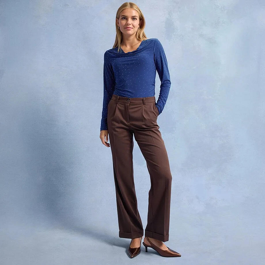 Blaues Langarmshirt mit Punkten, braune Hose mit weitem Bein und spitze braune Schuhe.