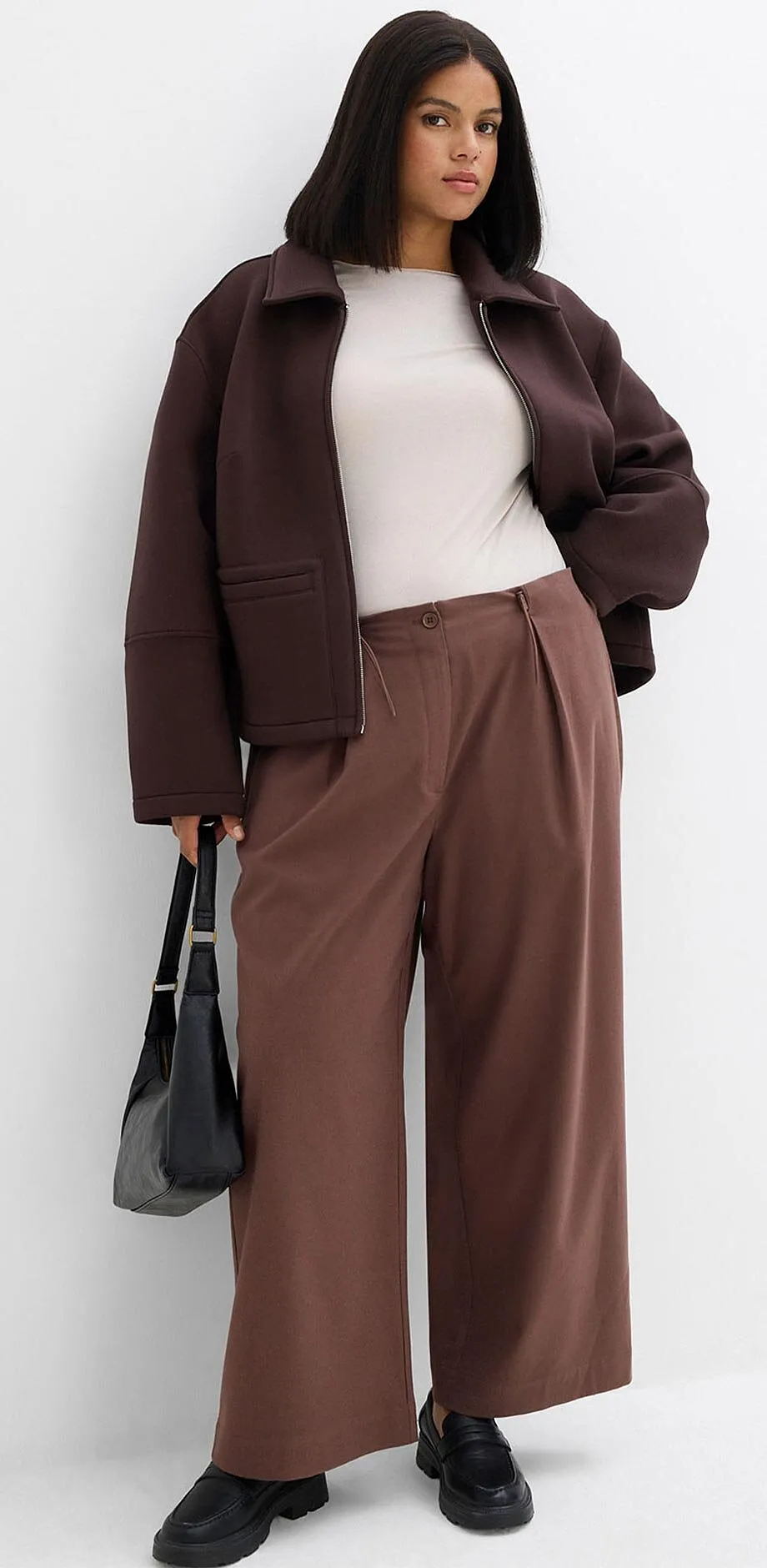 Braune Jacke, weißes Top und weite Hose in Erdtönen.