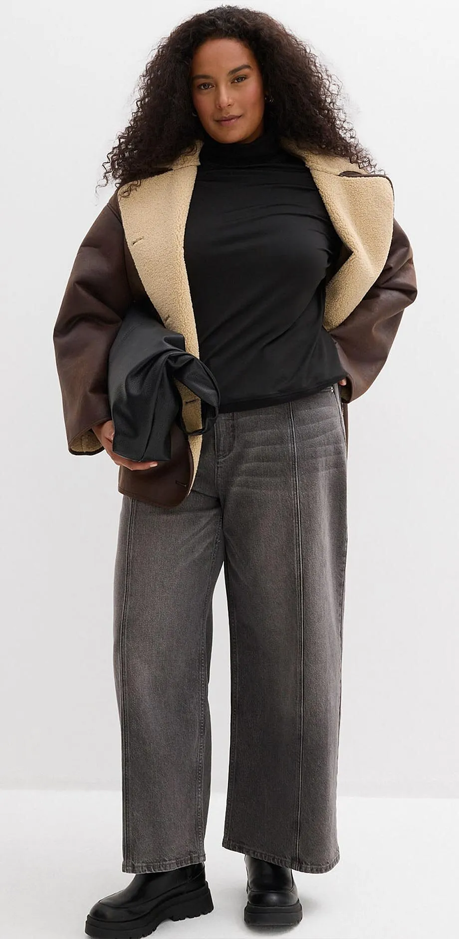 Jacke mit Fellkragen, schwarzer Rollkragenpullover und weite graue Hose.