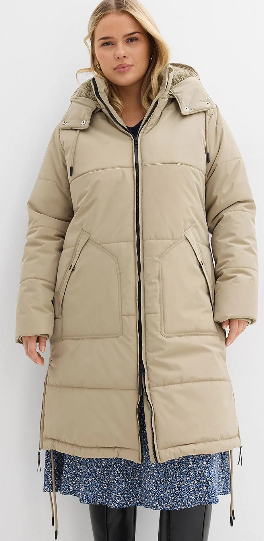 Beiger Steppmantel mit Kapuze über blauem Blumenkleid. 